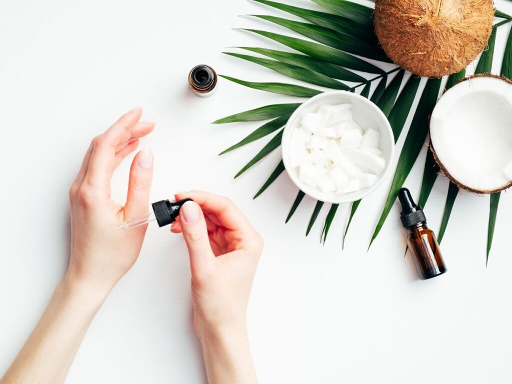 hands applying essential oil with coconut oil in background and palm leaf on table