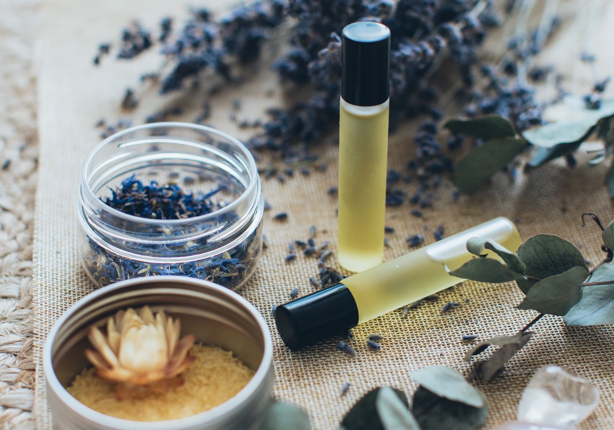 essential oil roller and dried herbs in clear bowls