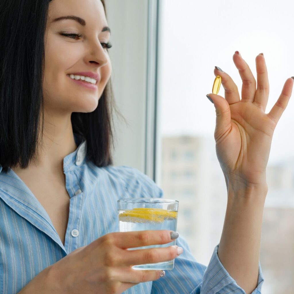 woman ingesting an essential oil veggie capsule with lemon water in her hand