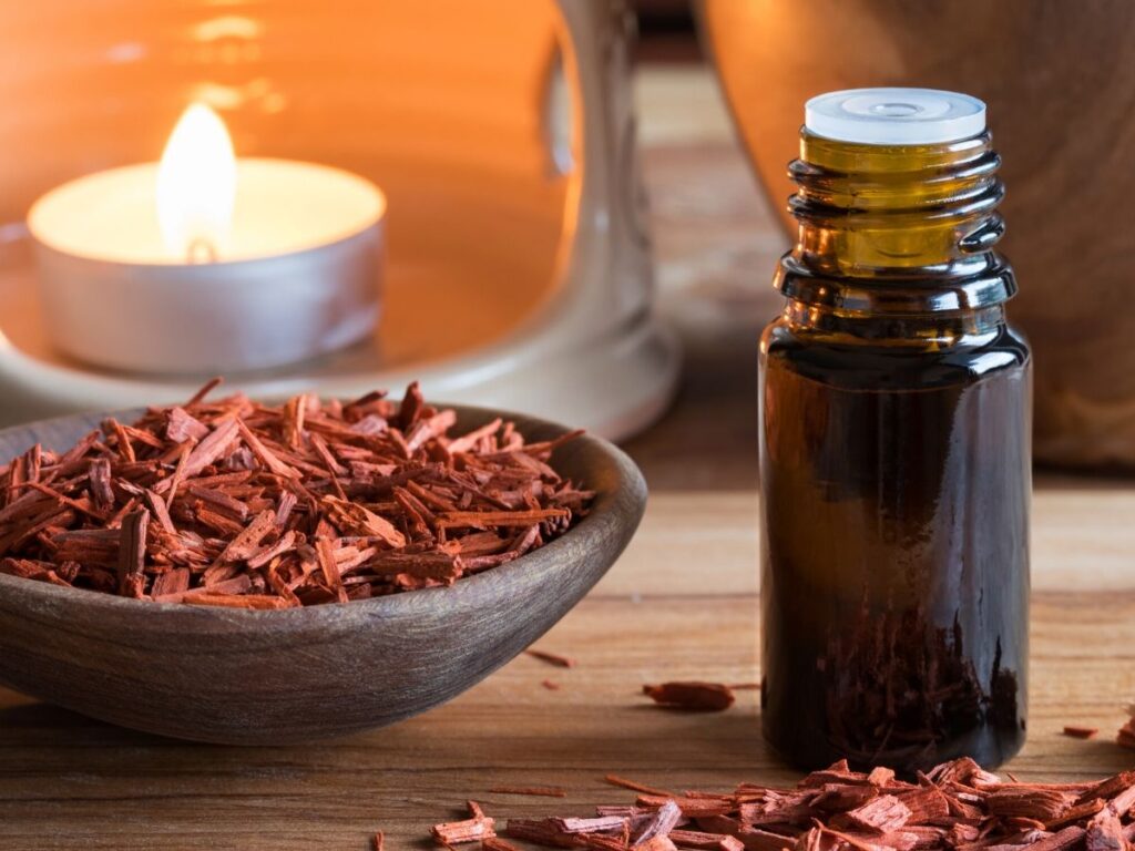 sandalwood essential oil bottle with sandalwood chips in a bowl and a candle behind it