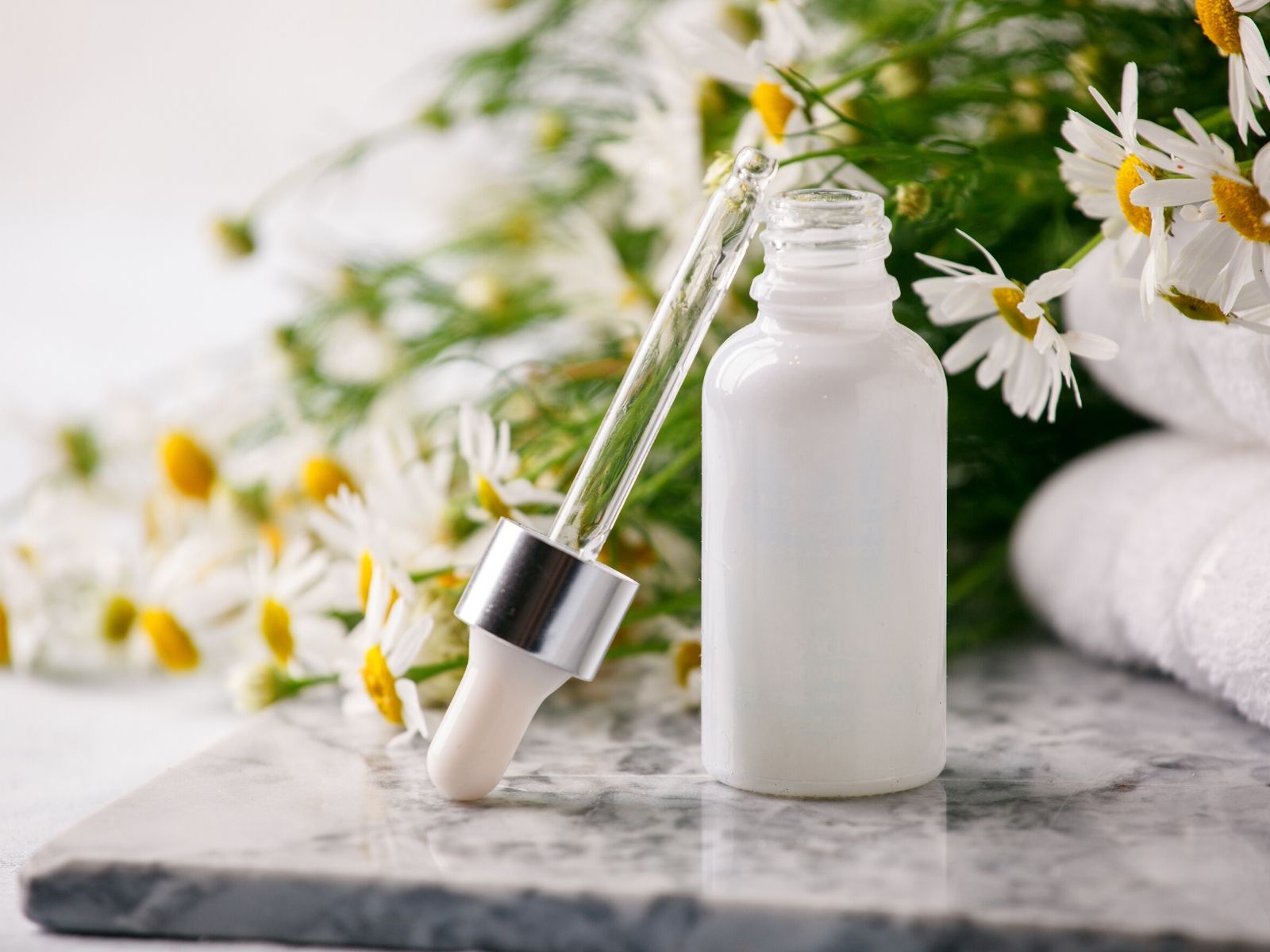 white essential oil bottle with flowers in the background.