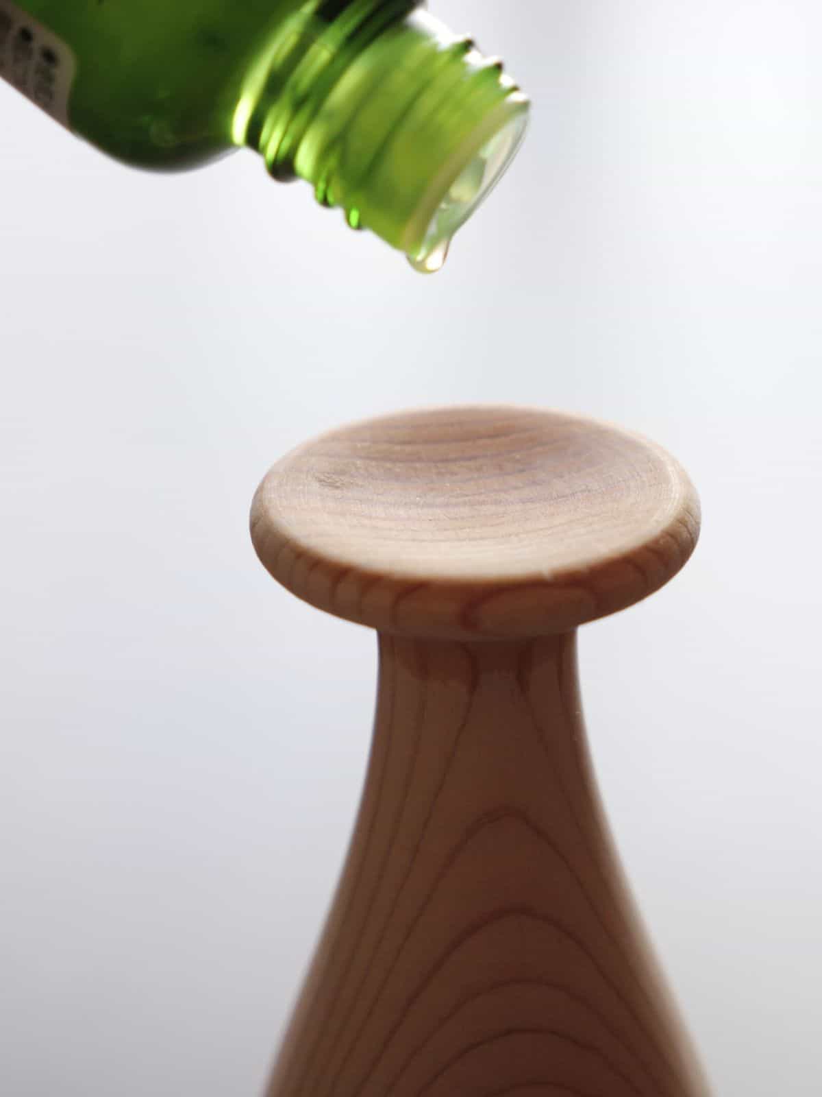 Wooden diffuser on table with essential oil dripping onto it.