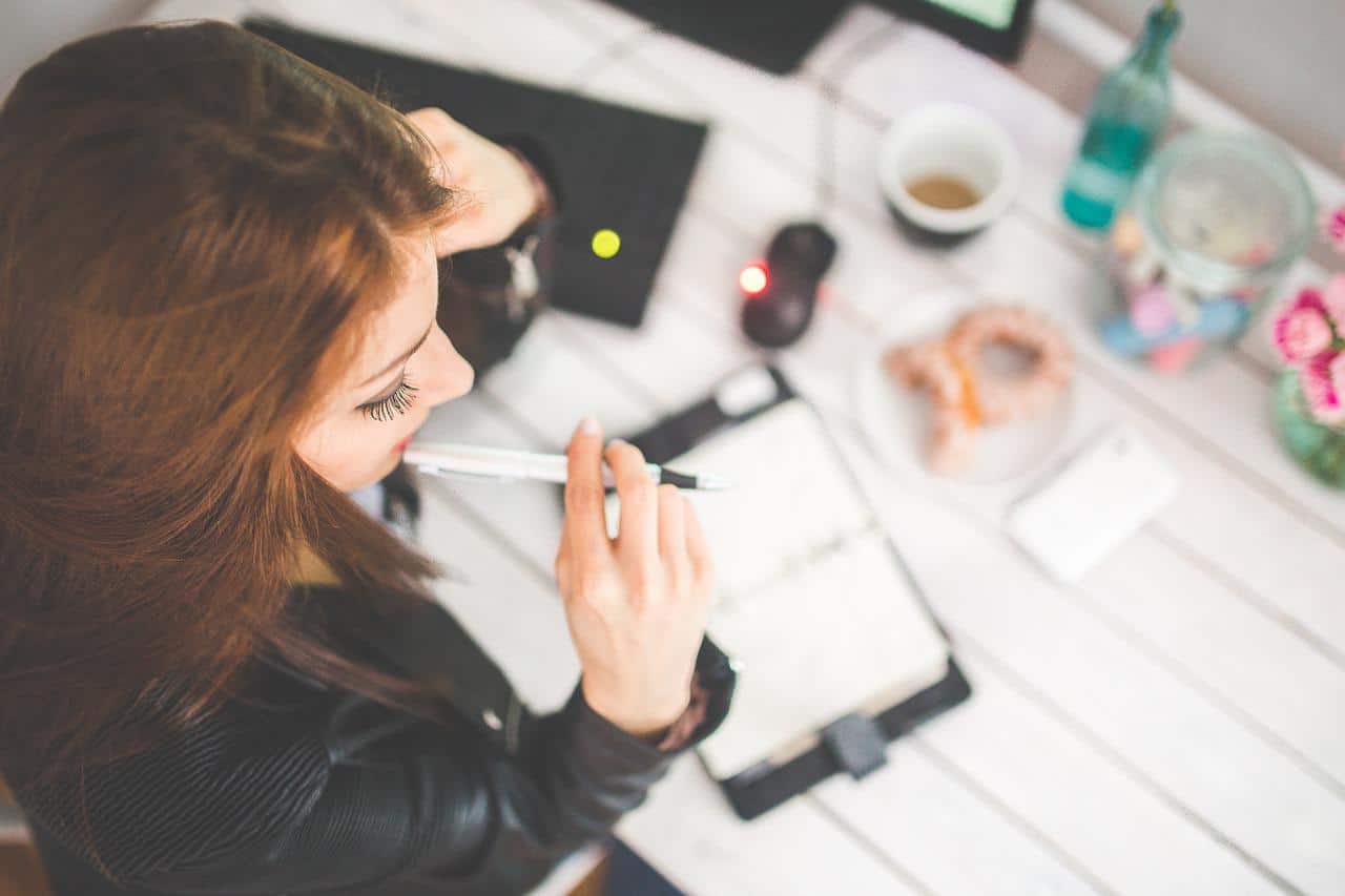 A young woman sits thinking over her planner.